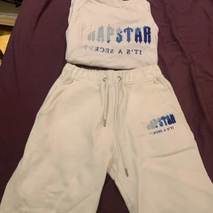 Trapstar set  - Säljer en vit t-shirt och shorts från Trapstar med texten 'IT'S A SECRET' i blått och vitt. Perfekt för en avslappnad stil eller streetwear-look. T-shirten är i bra skick och redo för nya äventyr. Passar perfekt till sommaren eller våren!