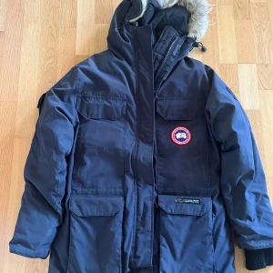 Canada Goose expedition jacka/parka - Den har några år på nacken. Den har legat i garderoben de senaste 7 åren. Bra skick. Mörkblå. Storlek M.  Liten slitning på kanten av en ficka. Syns mer på bilden än i verkligheten. En söm har gått upp 1 cm på en ärm. Noppriga muddar, tas lätt bort. 