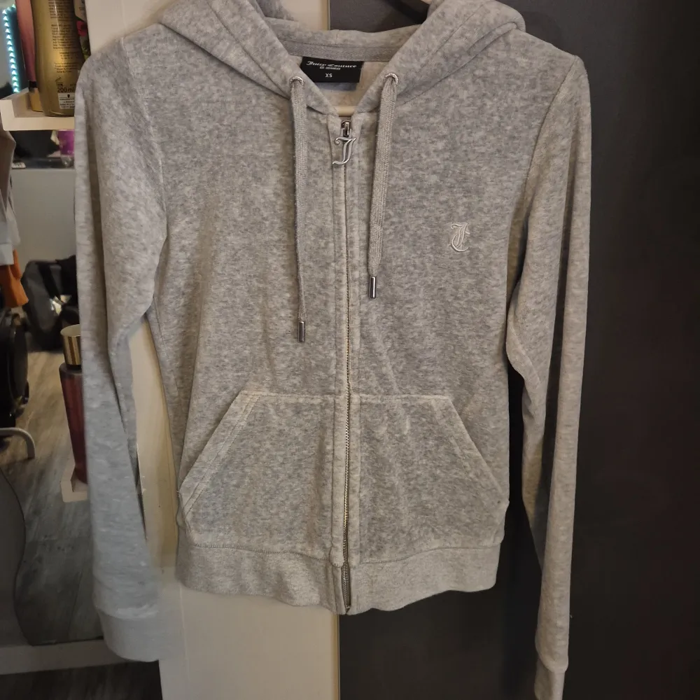 Säljer en supermjuk och bekväm grå hoodie från Juicy Couture. Den har en dragkedja framtill och en klassisk huva med snören. Perfekt för en avslappnad stil eller mysiga dagar hemma. Den är i nyskick och redo för en ny ägare!. Tröjor & Koftor.