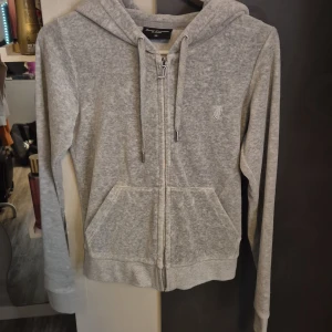 Grå hoodie från Juicy Couture - Säljer en supermjuk och bekväm grå hoodie från Juicy Couture. Den har en dragkedja framtill och en klassisk huva med snören. Perfekt för en avslappnad stil eller mysiga dagar hemma. Den är i nyskick och redo för en ny ägare!