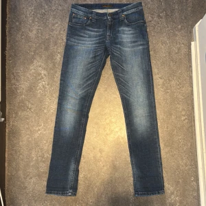 Blå jeans från Nudie - Säljer ett par snygga blå jeans från Nudie. De har en klassisk femficksdesign och en bekväm passform. Storlek 29/32 och modellen är ”Tight Long John”☑️