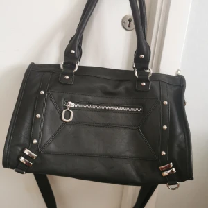 Svart handväska från Charmant of Sweden - Snygg svart handväska i syntet från Charmant of Sweden. Väskan har silverfärgade detaljer och en praktisk dragkedja framtill.    Mycket bra skick🌸