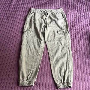 Olivgröna cargobyxor från 157 - Säljer ett par grön cargobyxor från 157 i storlek S. Byxorna har flera praktiska fickor och elastiska muddar vid bensluten. Perfekta för en avslappnad stil och passar till många olika tillfällen. De är i bra skick och redo för nya äventyr!