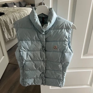 Unisex Moncler Väst - jättesnygg och unik vintage ljusblå moncler väst. storlek: 2 / M men passar S. defekter:  fyra små fläckar vänster sida av halsen men de är inget man märker direkt och kan lätt tas bort med rätt produkter. har två fickor på värje sida. äkta såklart 