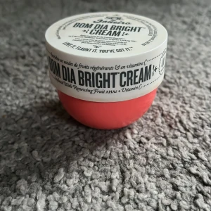Bom Dia Bright Cream från Sol de Janeiro - Säljer en härlig Bom Dia Bright Cream från Sol de Janeiro. Den kommer i en snygg, rund burk med en ljusrosa bas och vit lock. Krämen är berikad med fruktiga AHAs och vitamin C för en strålande hud. Perfekt för att ge huden en uppfriskande boost!