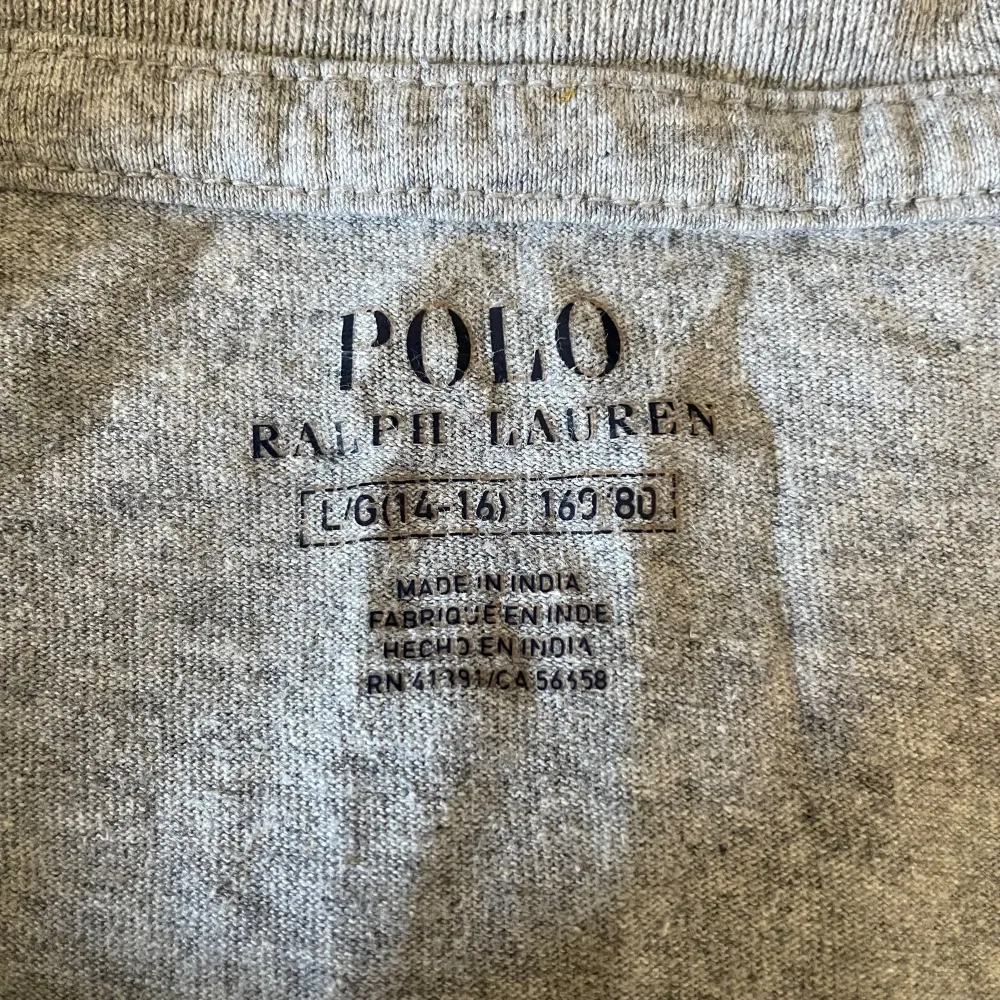 Säljer en snygg grå t-shirt från Ralph Lauren. Den har en klassisk design med en mörkblå broderad logga på bröstet och siffran 3 på ärmen. T-shirten är i bomull. Skick 7/10 eftersom att det är en jätte liten defekt i armhålan därför så lågt pris.. T-shirts.