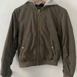 Bomberjacka  - Bomberjacka barn, gott skick (liten fläck på framsidan inte något som syns jättetydligts). Guldiga detaljer (dragkedja & knappar). Avtagbar luva. 