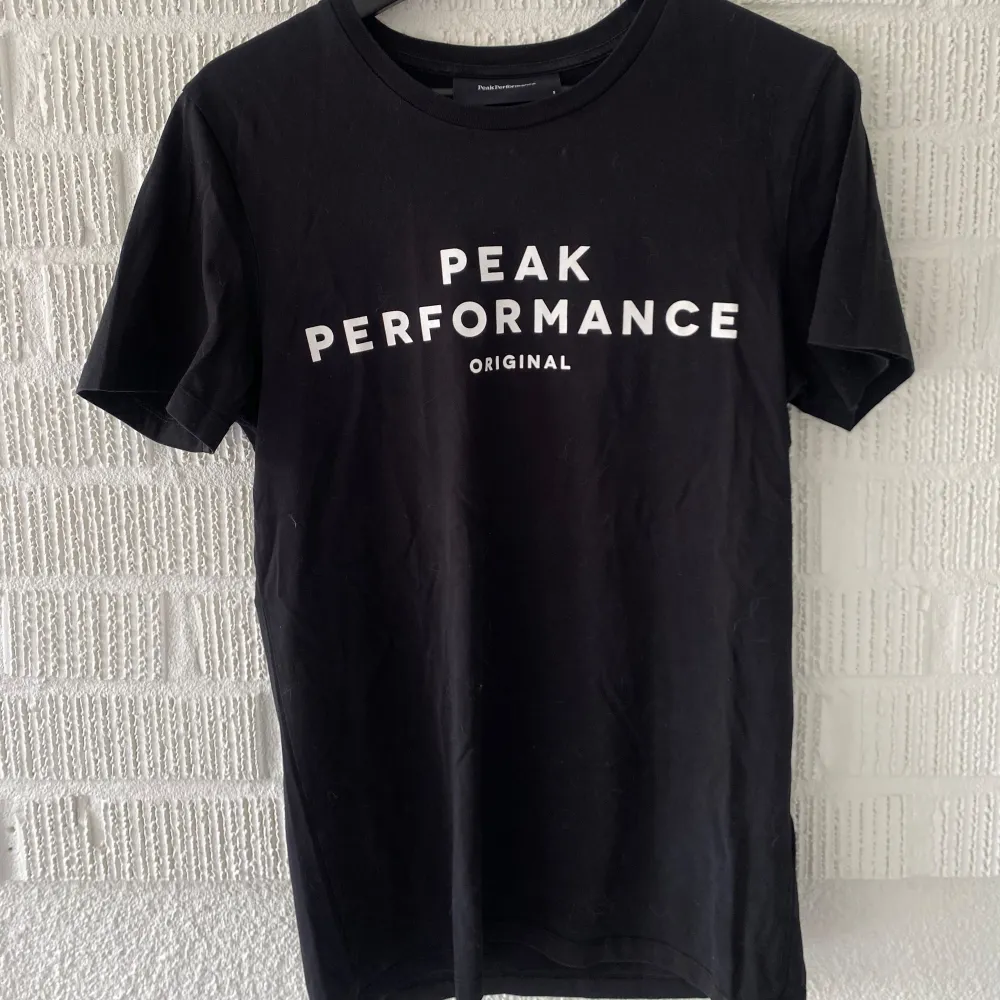 Säljer en stilren svart t-shirt från Peak Performance i storlek S. Den har en klassisk rund hals och korta ärmar. På framsidan finns en vit logotyp med texten 'Peak Performance Original'.. T-shirts.