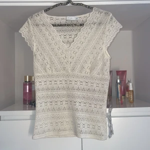 Beige spetsblus från Vila - Säljer en superfin beige spetsblus från Vila. Den har en v-ringad design och korta ärmar. Perfekt för både vardag och fest! Blusen är i ett vackert spetsmaterial som ger en romantisk känsla.