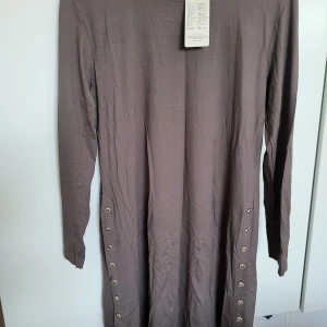 Klänning  - En långärmad klänning med knappar på ena sidan. Klänningen har en rund halsringning och är löst sittande.