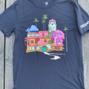 Tshirt med tryck - Svart Tshirt med tryck fram Och på ärmen: encanto. Använd några gånger men ok skick