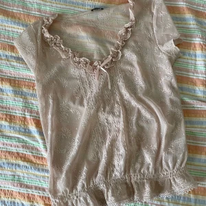 Beige spetsblus från Mexx - Säljer en superfin beige spetsblus från Mexx. Den har korta ärmar och en söt volangdetalj vid halsringningen. Perfekt för en somrig look eller en festlig kväll. Blusen är i ett lätt och luftigt material som känns skönt mot huden.