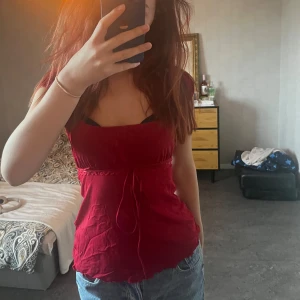 Röd topp med knytband - Säljer en snygg röd topp med knytband i midjan. Toppen har korta ärmar och en smickrande passform. Perfekt för en utekväll eller en avslappnad dag. Den är i bra skick och redo för en ny ägare! pris kan diskuteras vid snabbt köp🩷