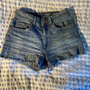 Blå jeansshorts från Lindex - Säljer ett par snygga blå jeansshorts från Lindex i storlek EUR 34. De har en vintage-look med fransiga kanter och klassisk femficksdesign. Perfekta för sommardagar eller festivaler! 🕶️