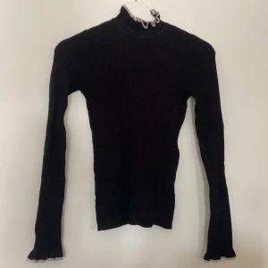 Svart stickad polotröja från Gina Tricot - Säljer en snygg svart stickad polotröja från Gina Tricot i storlek XS. Tröjan har långa ärmar och en fin ribbad struktur. Den har också en stilren vit kantdetalj vid ärmslut och krage som ger en extra touch. Perfekt för höst och vinter!