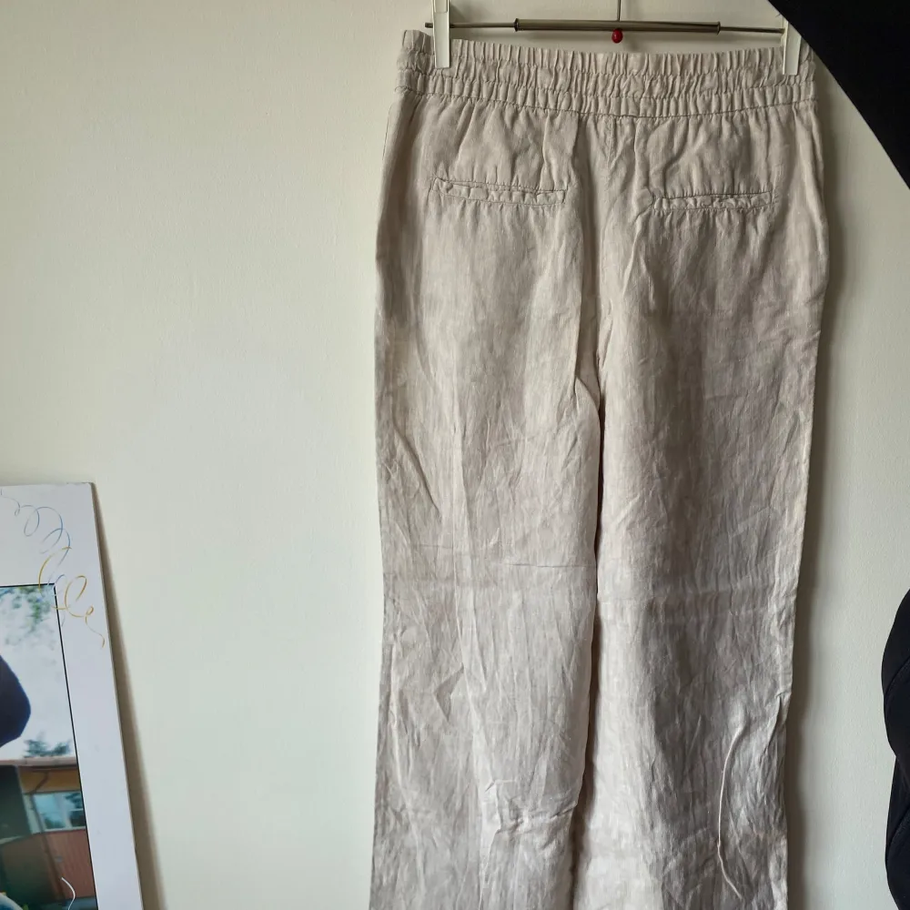 Säljer ett par snygga beige linnebyxor. De är högmidjade och har en avslappnad passform med breda ben. Perfekta för sommaren med sitt lätta och luftiga material. Byxorna har elastisk midja för extra komfort.. Farkut & Housut.