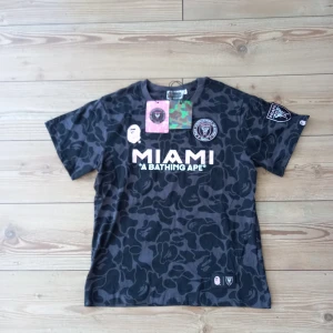 Fotbollströja Inter Miami Bape - Säljer nu den hära jättesnygga Inter Miami fotbollströja när dem collabade tillsammans med märket A Bathing Ape. Skick: 10/10, alla lappar finns kvar. Storlek: M Tyget är inte som en vanlig fotbollströja, det är gjort av bommul.