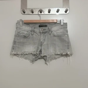 Grå jeansshorts från Levi's - Säljer ett par grå jeansshorts från Levi's, modell 524 Too Superlow. De är lågmidjade och har en snygg fransig kant nedtill. Perfekta för sommaren och ger en avslappnad look. Passar bra till både vardag och fest!