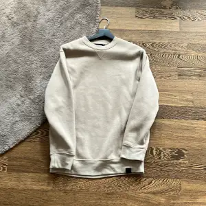 Säljer en stilren beige sweatshirt i normal passform. Den är långärmad och perfekt för både höst och vår. Materialet känns mjukt och skönt mot huden. Enkelt att matcha med olika outfits!