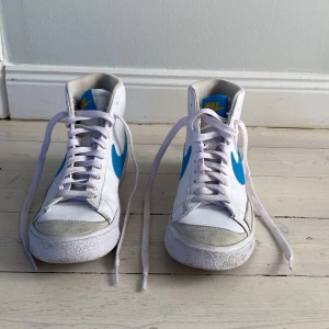 Nike skor - Nike modell blazer mid, mellanhöga skor vita med blå swoosh och beige bakflik med gul text storlek 36,5  nästan helt oanvända
