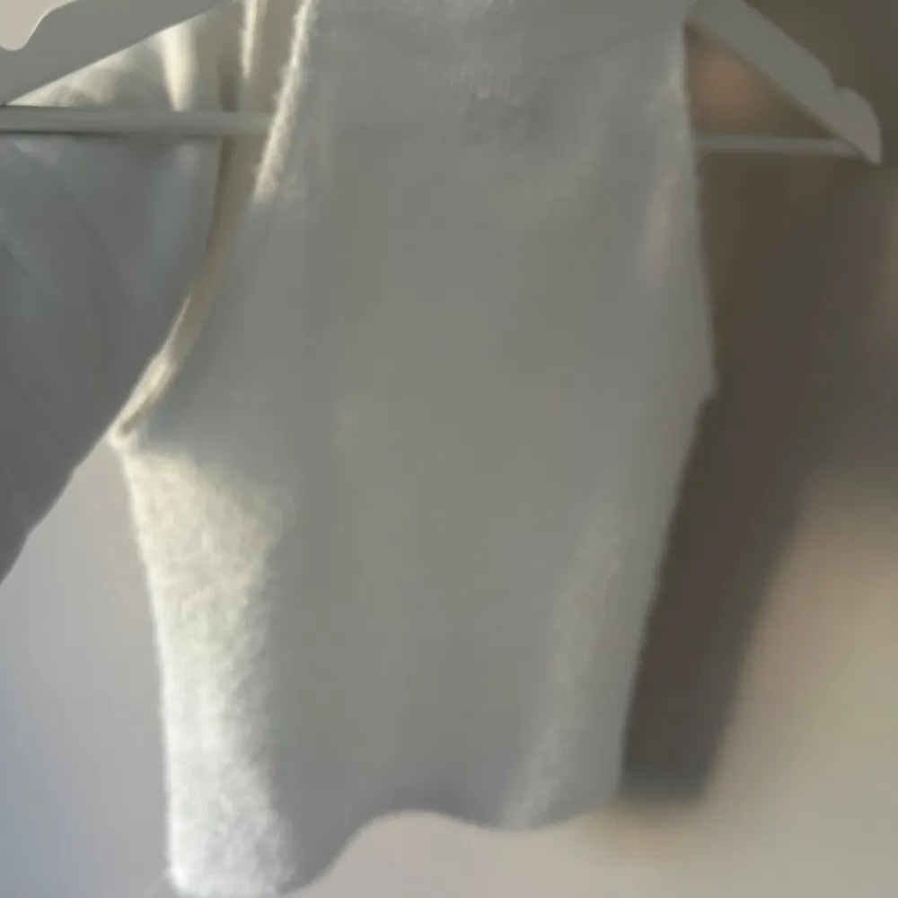 Säljer en superfin vit ärmlös stickad topp. Den är mjuk och fluffig, perfekt för både vardag och fest. Toppen har en hög hals och är i ett mysigt material som känns skönt mot huden. Passar perfekt till höst- och vintergarderoben! Är lite genomskinlig men inte om man har ex hudfärgad bh. Yläosat.