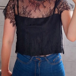 Svart spetsblus med korta ärmar - Säljer en elegant svart spetsblus med korta ärmar. Blusen har en genomskinlig spetsdesign med ett underlinne som täcker bröstområdet. Perfekt för en festlig kväll eller en utekväll med vänner. Blusen är i fint skick. Strl M men liten, passar mig med storlek XS-S. 