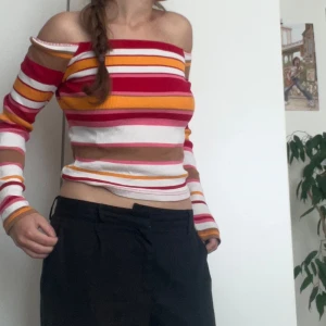 Randig offshoulder topp från BikBok - Säljer en superfin randig offshoulder topp från BikBok i storlek S. Toppen har ett färgglatt mönster med ränder i rött, vitt, gult och beige. Den är ribbad och har långa ärmar. Perfekt för både vardag och fest!