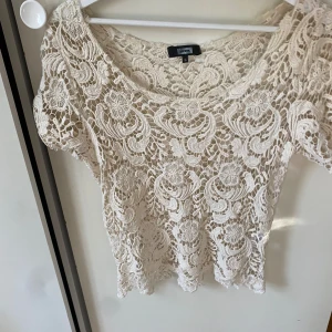 Beige spetsblus från Bik Bok - Säljer en superfin beige spetsblus från Bik Bok. Den är kortärmad och har ett vackert mönster med blommor och virvlar. Perfekt för sommarens fester eller en dag på stan. Blusen är i nyskick och har en normal passform. Passar perfekt till både jeans och kjol!