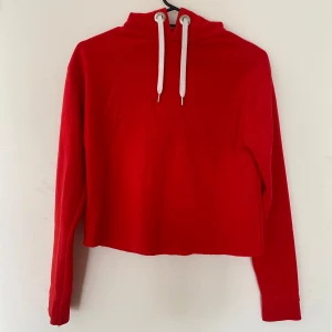 Röd croppad hoodie - Säljer en snygg röd croppad hoodie med vita snören. Den är perfekt för höst och vinter, och är supermysig att ha på sig. Hoodien har långa ärmar och en luva som gör den extra bekväm. Passar perfekt till både vardag och chillkvällar. Köp direkt eller ge prisförslag 💛