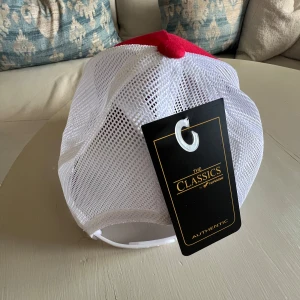 Röd och vit snapback keps från Yupoong - Säljer en snygg röd och vit snapback keps från Yupoong. Kepsen har en röd front med broderad text 'DMC' och vit mesh på baksidan för bra ventilation.  Kepsen är i nyskick och har en justerbar passform.