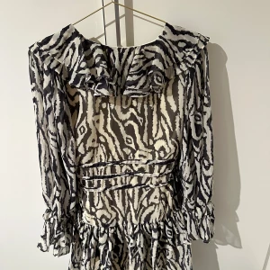 Zebramönstrad klänning från Topshop - Oanvänd zebramönstrad klänning från Boohoo, Den är svart och vit med volanger. Klänningen har långa ärmar.