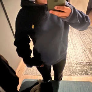 Mörkblå hoodie från Ralph Lauren - Säljer en snygg och bekväm mörkblå hoodie från Ralph Lauren. Den har en klassisk design med en liten gul logga på bröstet. Hoodien är i bra skick och supermjuk. Perfekt för att hålla sig varm och stilig! 💙