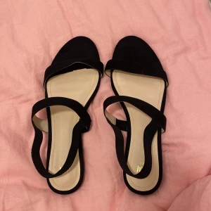 Svarta sandaler från H&M - Säljer ett par svarta sandaler från H&M i storlek 41. De är i syntetmaterial med en enkel och stilren design. Perfekta för sommaren och passar till både vardag och fest. De har en bekväm passform med en rem över foten och en runt hälen. Aldrig änvändt de, pga att de är för stora. Men köpte de på sellpy!🌟