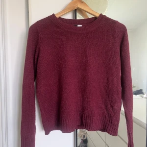 Vinröd stickad tröja - Säljer en mysig vinröd stickad tröja. Den är perfekt för höst och vinter med sin varma och sköna känsla. Tröjan har långa ärmar och en ribbad nederkant som ger en snygg passform. Perfekt för att hålla sig varm under kyliga dagar!