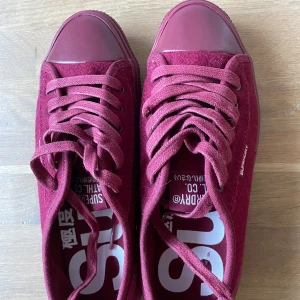 Superdry sneakers  - Low Pro Luxe Trainers i färg vinröd (Deep Berry). Den är storlek EU37 men liten i storleken därför säljs dem. Aldrig använt och skokartongen finns kvar. På Superdry hemsidan pris £34,99. Skriv om mer bilder önskas. Köpare betalar frakten. 
