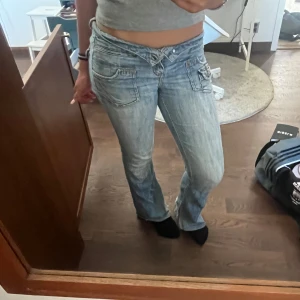 Lågmidjade jeans från Paris Blues - Säljer ett par snygga lågmidjade jeans från Paris Blues i storlek S. De är ljusblåa med en sliten look och har en bootcut-stil. Jeansen har knappar och dragkedja framtill samt fickor både fram och bak.  Priset kan diskuteras, vill mest bli av med dem då de är för små tyvärr.