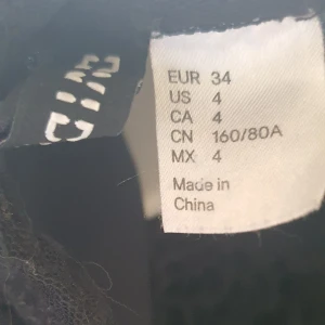 Svart klänning med spetsdetaljer - Säljer en elegant tröja i storlek XS. tröjan har korta ärmar och vackra spetsdetaljer där fram som ger en fin touch. Perfekt för festliga tillfällen eller en utekväll. tröjan är i medelskick och redo att bäras av någon som vill känna sig extra fin.