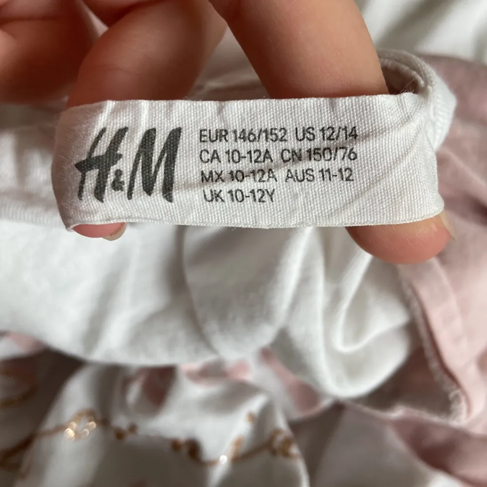 Säljer en söt t-shirt från H&M i storlek 146/152. Den är vit med rosa detaljer och har ett tryck på framsidan. T-shirten är kortärmad och gjord av bomull, perfekt för sommaren! Den är i bra skick och redo för en ny ägare. 🌸. T-shirts.