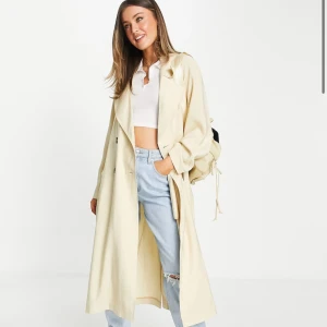 Beige trenchcoat - Säljer en snygg trenchcoat i storlek Xs.  Den är perfekt för vår och höst med sin klassiska design och knytskärp i midjan. Jackan har långa ärmar och två knappar framtill. Den är i bra skick och redo för en ny ägare. Egna bilderna är tagna i dåligt ljus så den är krämvit. 