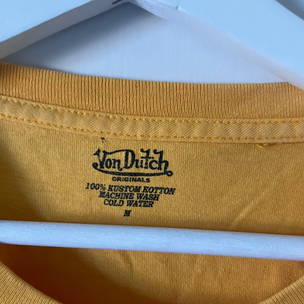 Säljer en cool gul t-shirt från Von Dutch. Den har flera broderade detaljer, inklusive en dödskalle och vingar. T-shirten är i bomull och har en normal passform. Perfekt för en avslappnad stil!. T-shirts.