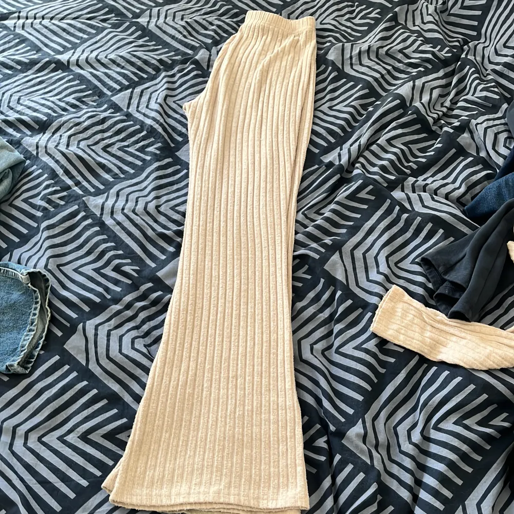 Säljer en superfin beige ribbad byxdress. Den är gjord av ett mjukt och stretchigt material som känns skönt mot huden. Byxdressen har långa ärmar och vida byxben, vilket ger en avslappnad och stilren look. Perfekt för både vardag och fest!. Muu.
