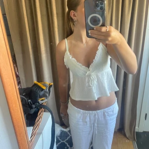 Vit spetslinne med volangdetaljer - Säljer ett superfint vit spetslinne med volangdetaljer.  Perfekt för sommardagar. Toppen är croppad och har en öppen rygg. Materialet är lätt och luftigt, vilket gör den bekväm att bära. Aldrig använd.