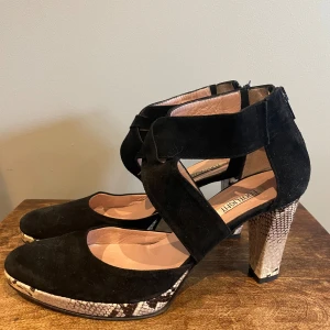 Svarta klackskor med ormskinnsmönster - Tuffa svarta klackskor i mocka och skinn med coolt ormskinnsmönster på klacken och sulan, elegant spetsig tå och en unik design med korsade remmar över foten. Perfekta för utekväll eller fest! 🖤🐍 Anv 1 gång på bröllop. Tillverkade i Italien. 