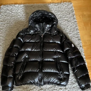 Moncler maya  - Säljer en snygg och varm svart pufferjacka från Moncler. Jackan har en glansig finish och är perfekt för kalla dagar. Den har en dragkedja framtill och långa ärmar. Perfekt för vintern! 🖤