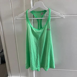 Grön linnetopp från Adidas - Säljer en fräsch grön linnetopp från Adidas. Perfekt för träning eller en varm sommardag. Toppen är ärmlös och har en bekväm passform med brottarrygg. Adidas-loggan syns diskret på framsidan. Materialet känns lätt och luftigt.