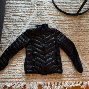 Svart pufferjacka - Säljer en svart pufferjacka i storlek M. Den är perfekt för kyliga dagar med sitt quiltade mönster och långa ärmar. Jackan har en dragkedja framtill och är i bra skick. 