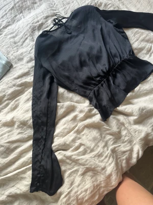 Blus - Svart blus med öppen rygg i storlek L från bikbok med knappar vid ärmen 