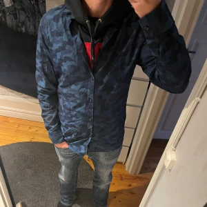  J.Lindeberg Camoskjorta - Kylig hoodie från J.Lindeberg i storlek M. Modellen är 174 och sitter stort. Perfekt att ha en hoodie under eller bara ha som vanlig skjorta.