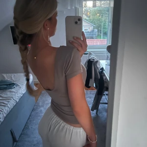 Beige tight topp - Säljer en beige tight topp med korta ärmar och u-ringning i ryggen. Toppen har en enkel och stilren design, perfekt för både vardag och fest. Materialet är mjukt och stretchigt, vilket gör den bekväm att bära. 