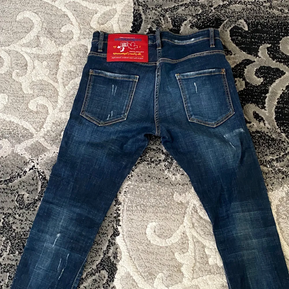 Säljer ett par snygga blå jeans från Dsquared2. De har en cool slitning och distressed look som ger dem en unik stil. Jeansen är i en klassisk blå färg och har en normal passform. Perfekta för en avslappnad vardagsstil!. Jeans & Byxor.